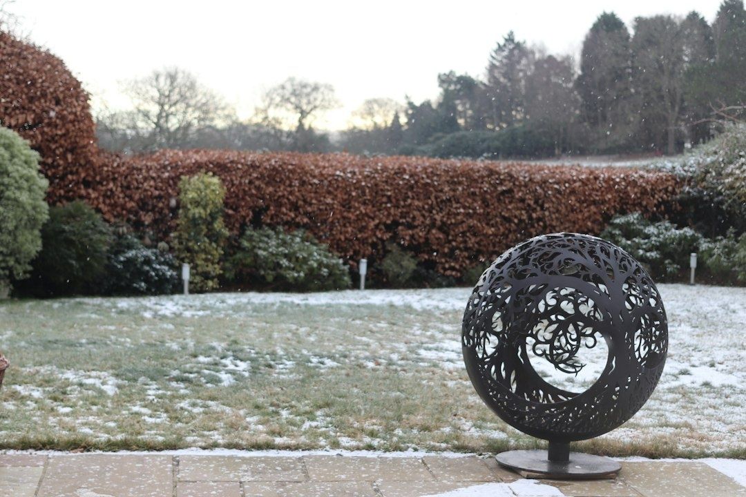 Ornate black metal sphere sculpture in a lightly snowy garden